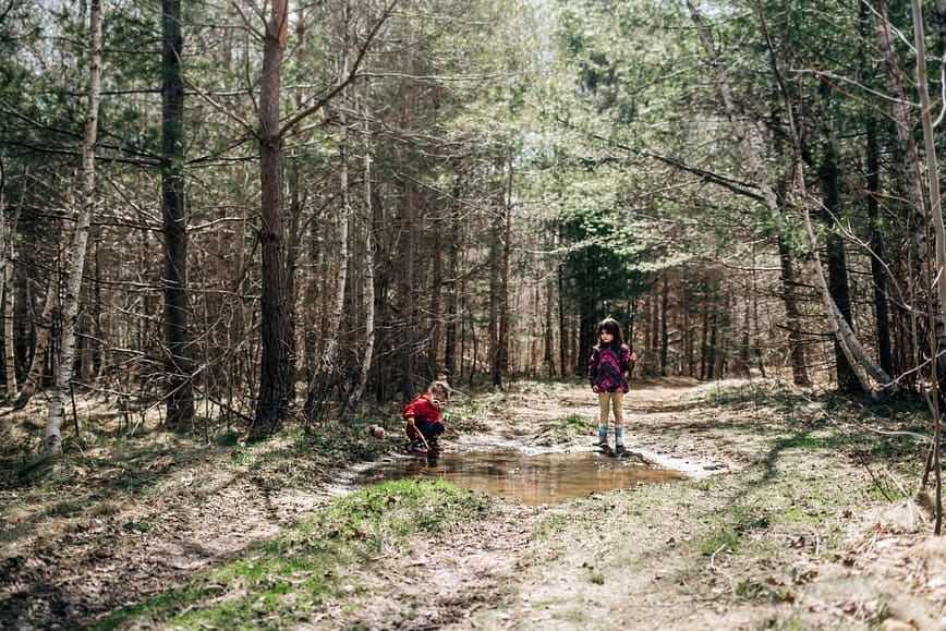 Children playing in the woods using their imagination to "fish" in a mud puddle