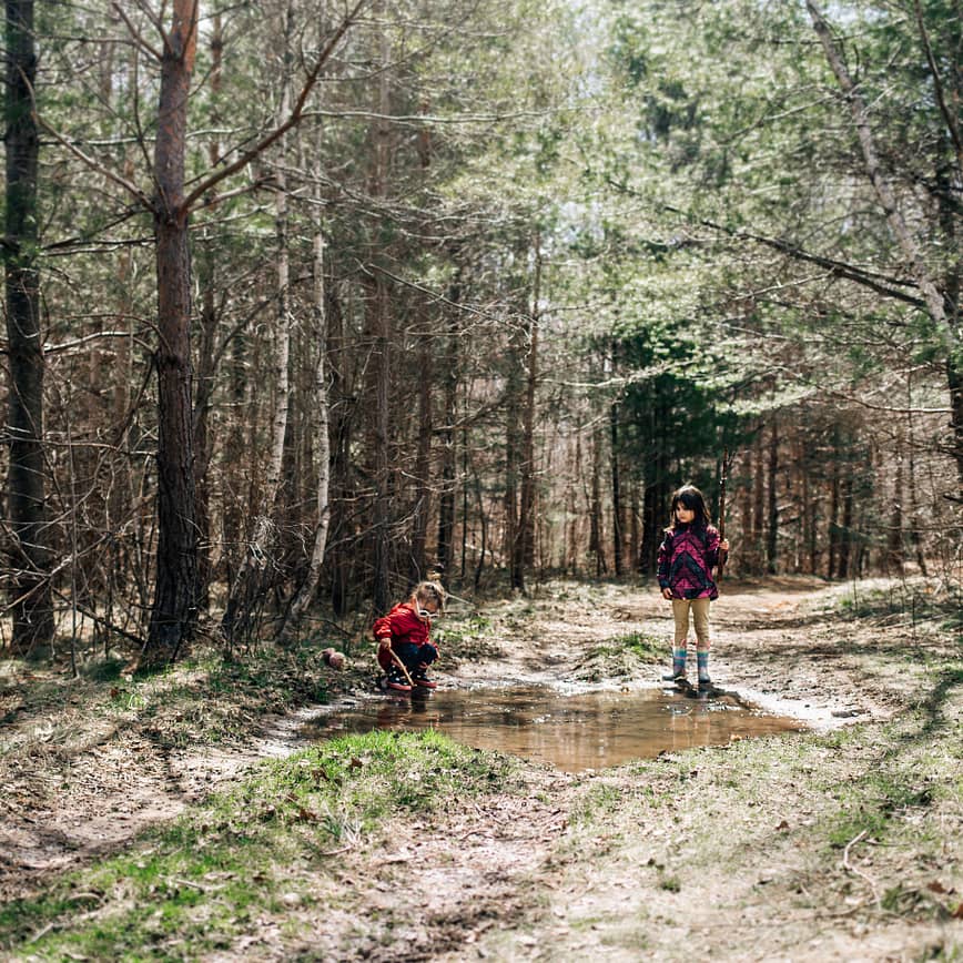 Children playing in the woods using their imagination to "fish" in a mud puddle
